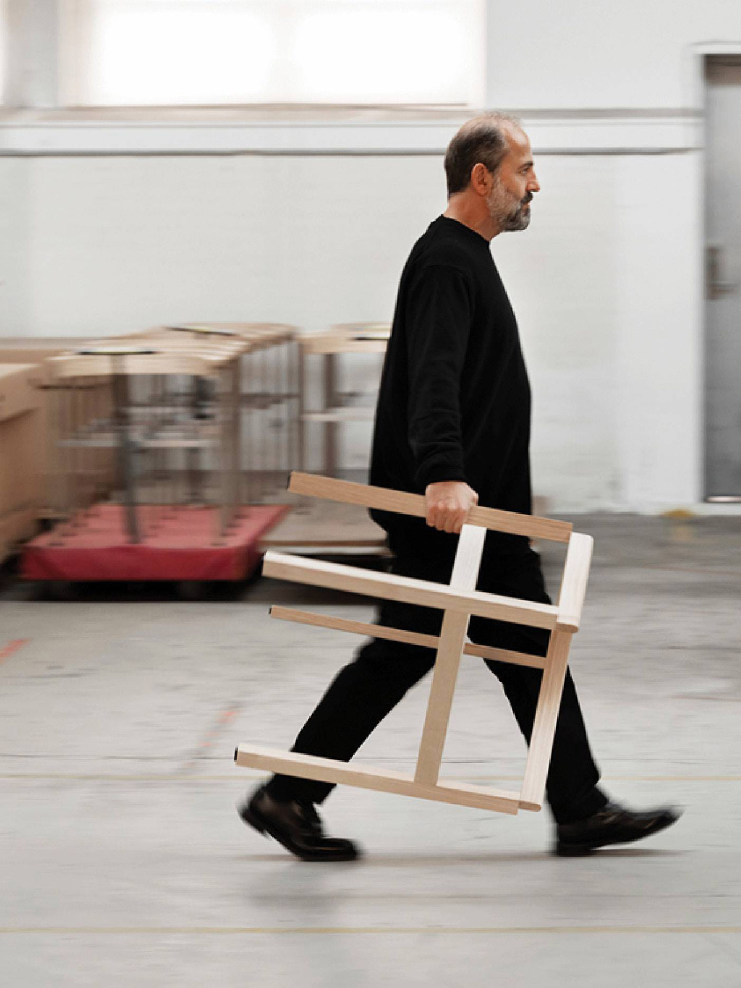 A man walking with a chair in his hand.