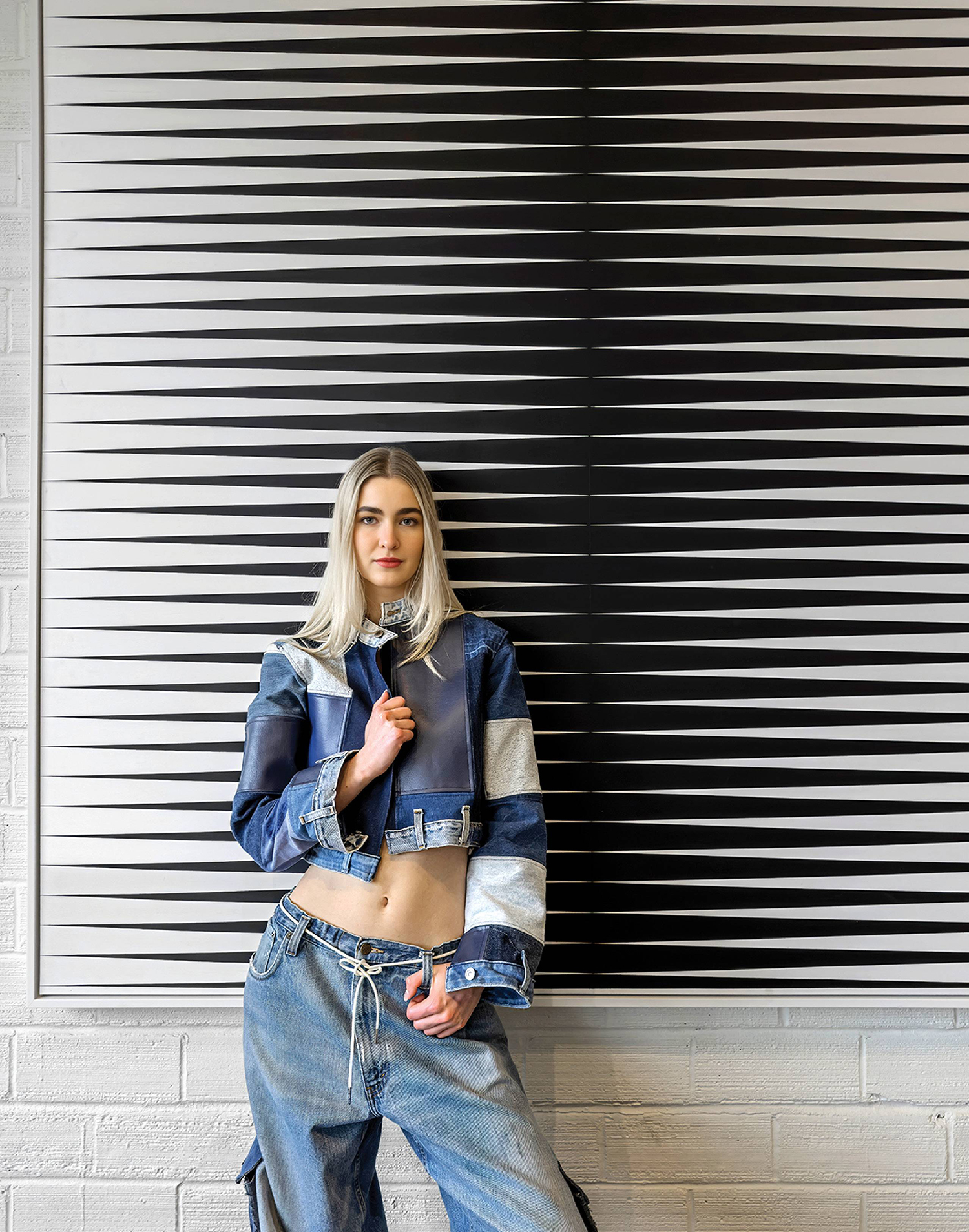 A woman in a denim jacket and jeans leaning against a wall