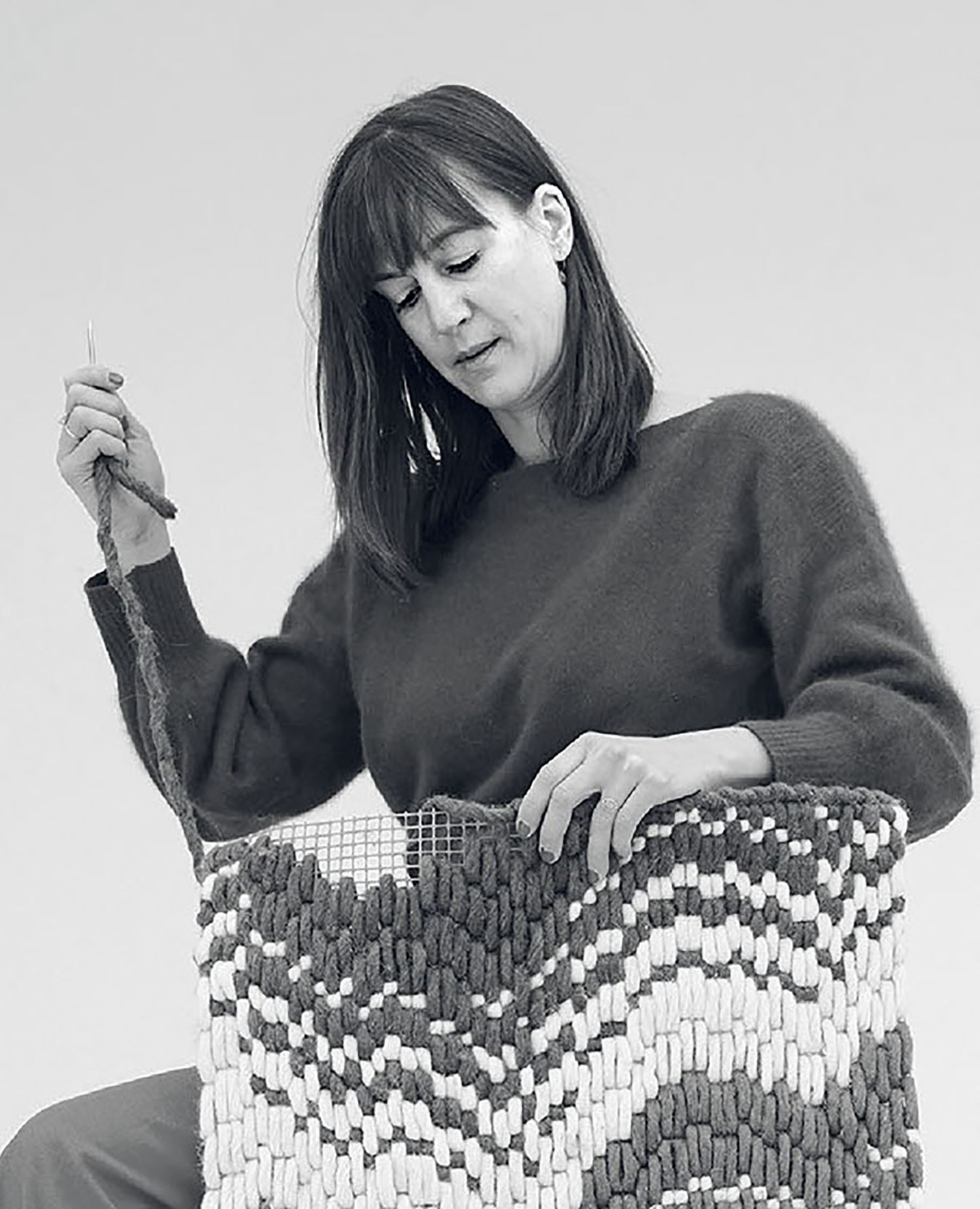 A woman sitting on a chair with a knitted bag.