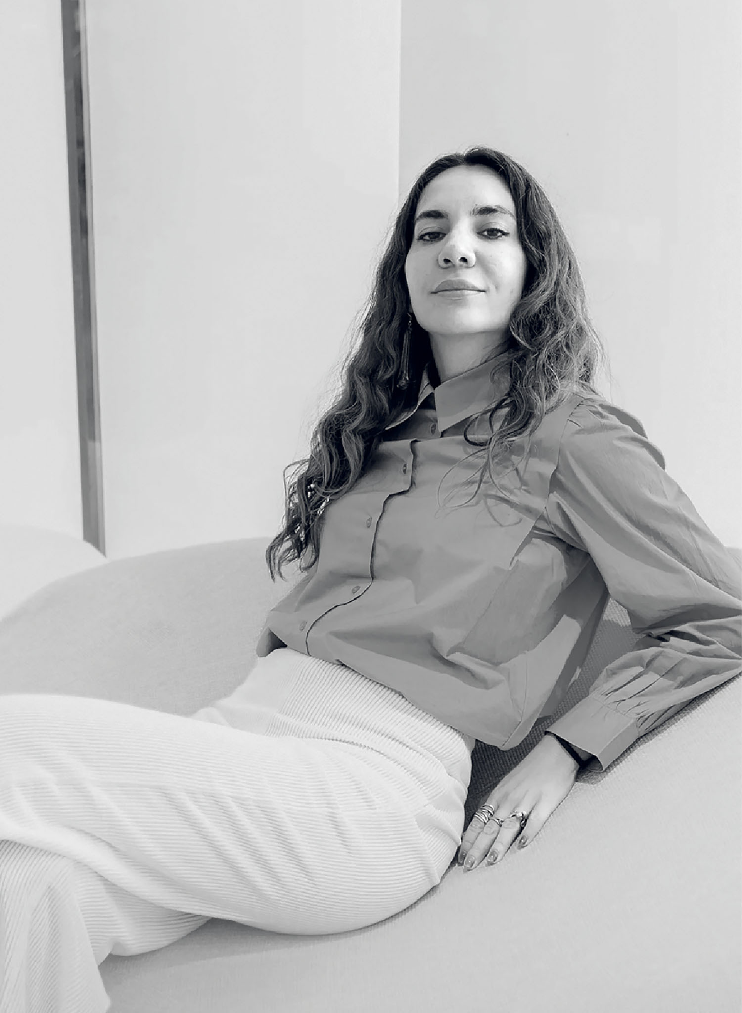 A woman sitting on a couch wearing a grey shirt and white pants.